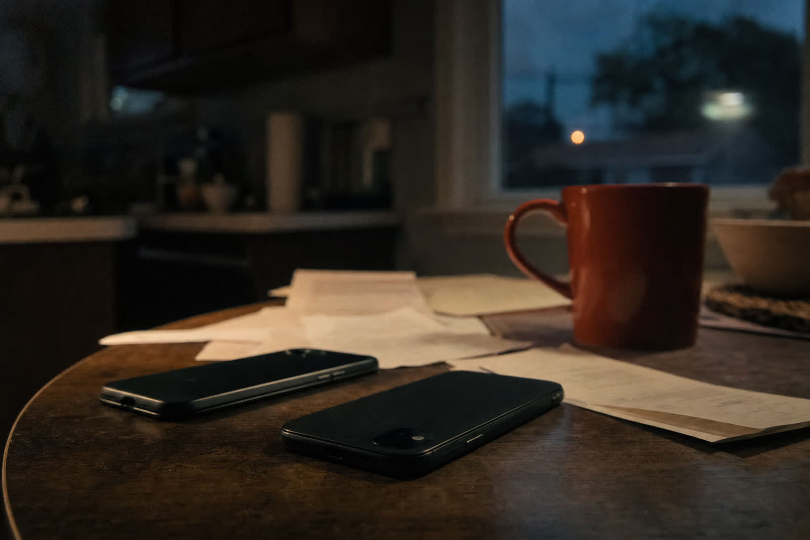 Illustrative scene, not a product screenshot: two phones face down on a kitchen table at night beside county notices