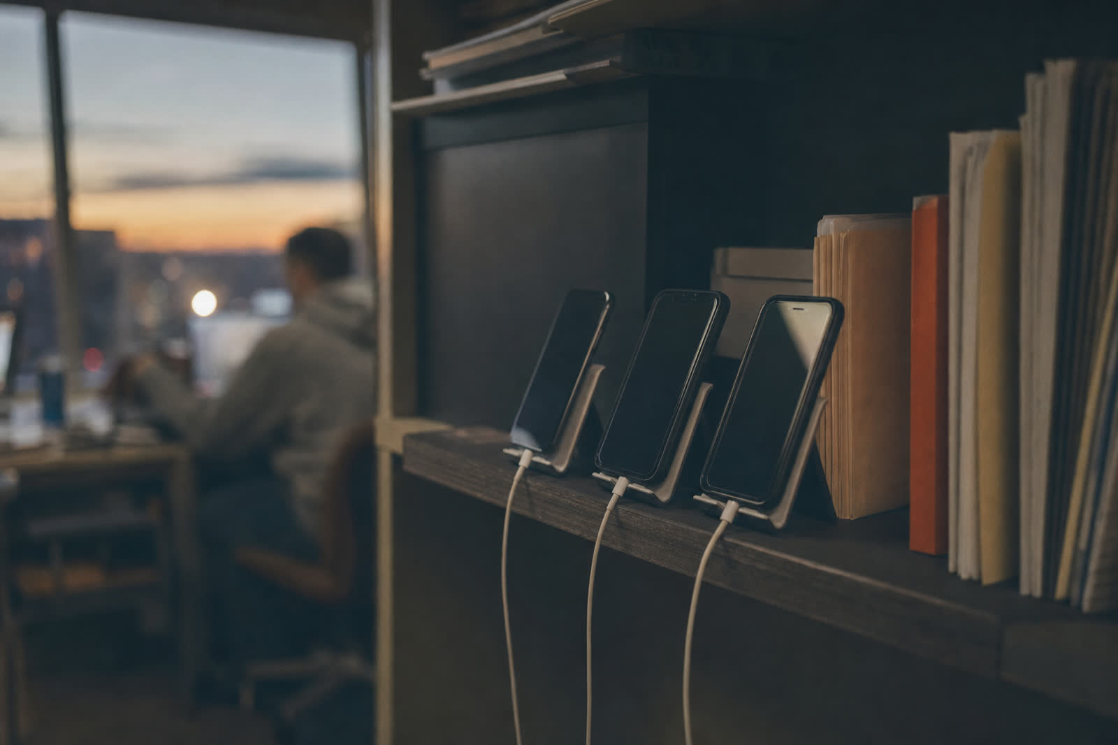 Illustrative scene, not a product screenshot: three phones charging side by side on a shelf in a small office